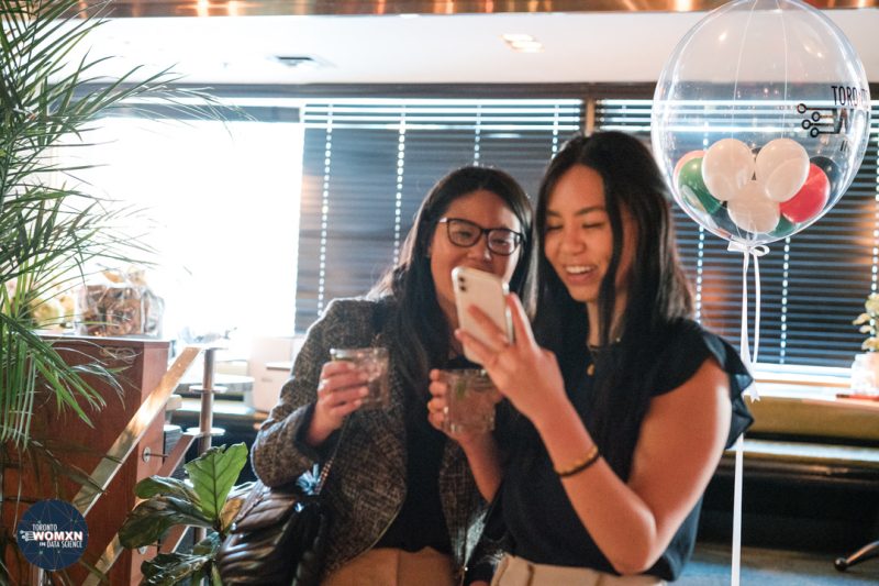 Corporate event photographer Toronto - two guests laughing at photos on a phone